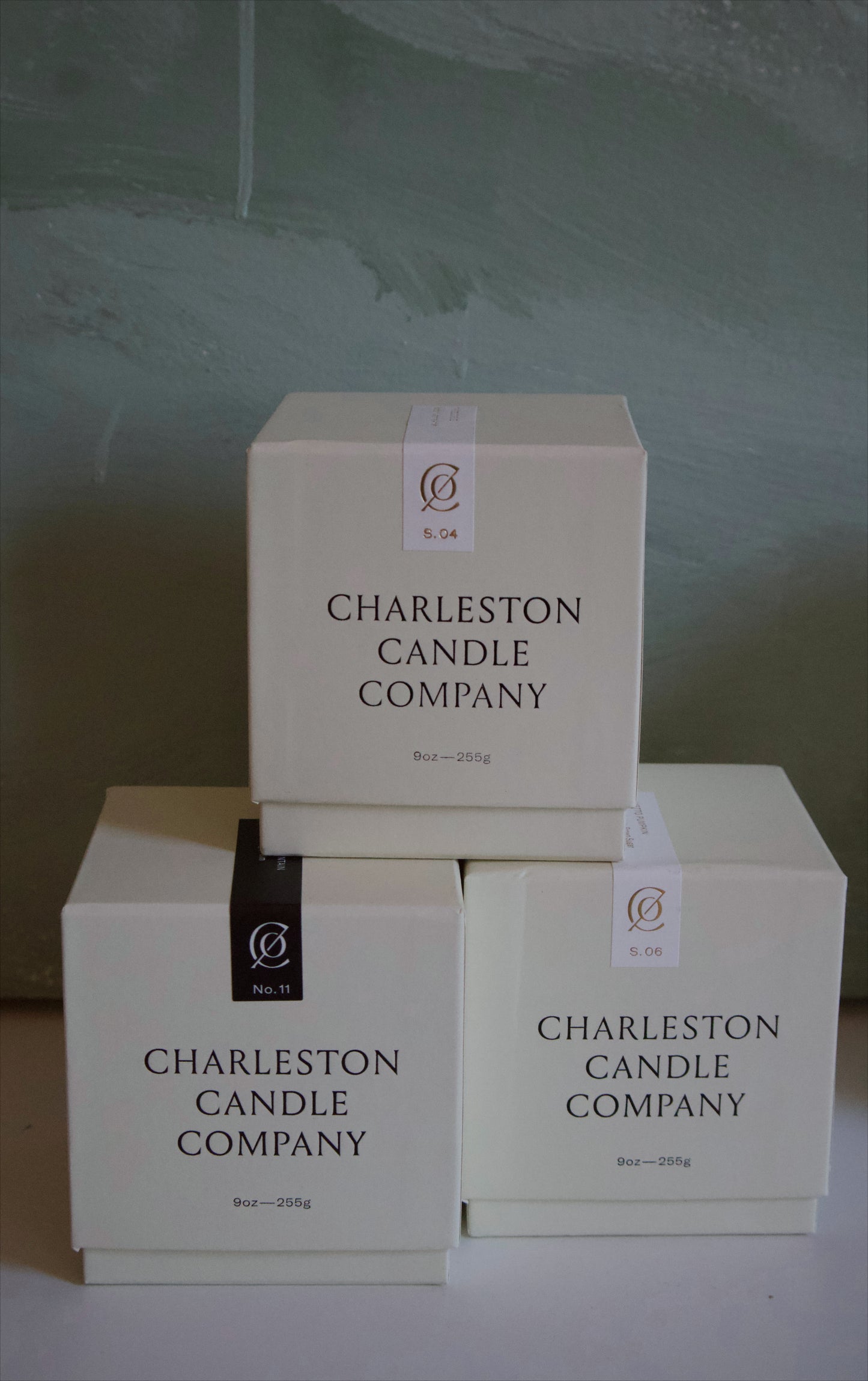 Three boxes from Charleston Candle Company stacked on a light surface with a textured white background.
